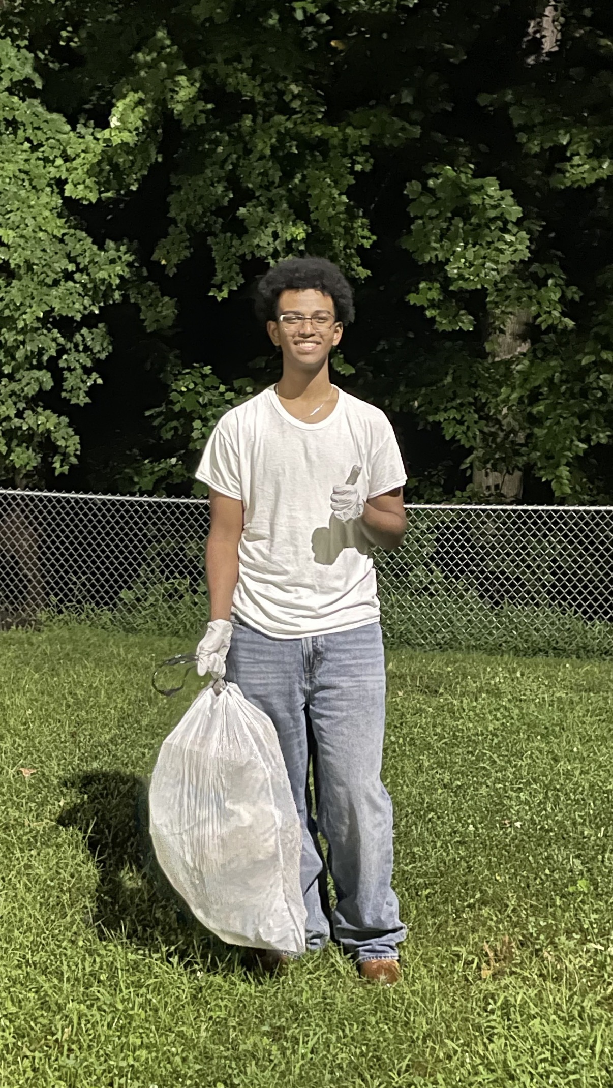 A person wearing gloves and holding a collection bag outdoors