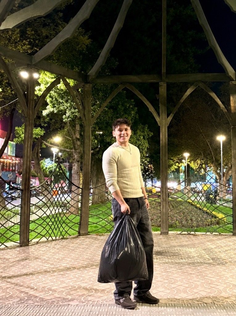 A person holding a large black bag beneath a garden pavilion